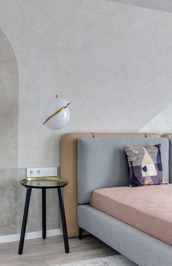 Comfortable bed with colorful pillow near bedside table under lamp with creative design